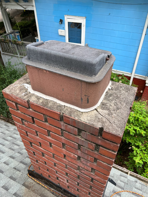 Gray chase cover sitting on a red brick chimney beside blue siding