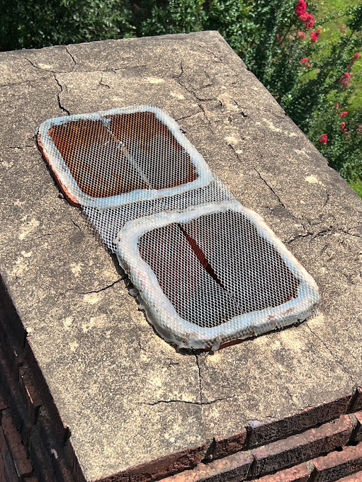 Two rusted mesh flue caps set into a cracked mortar crown