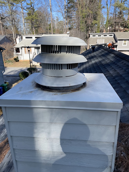 Multi-tier metal draft cap standing on a gray chimney chase cover