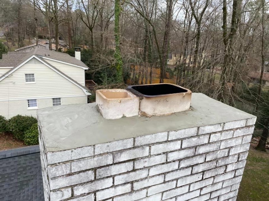 Chimney with a freshly finished mortar crown and two clay flue tiles above white painted brick
