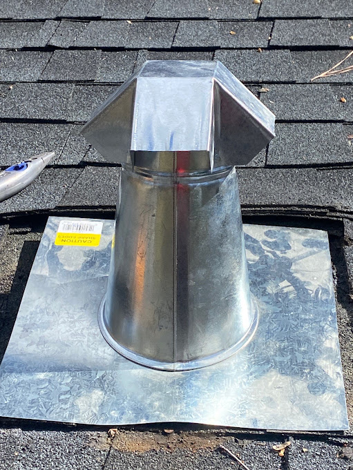 New galvanized B-vent flashing and storm collar set into a fresh flashing base during a roof repair