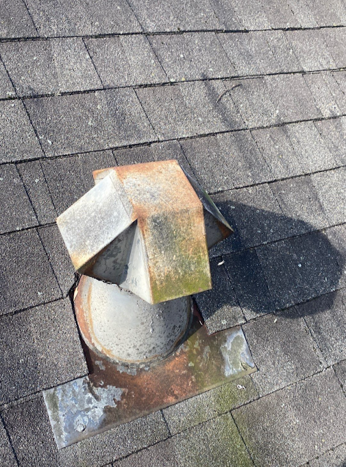 Corroded B-vent flashing peeled back from the roof deck with rust staining on the surrounding shingles