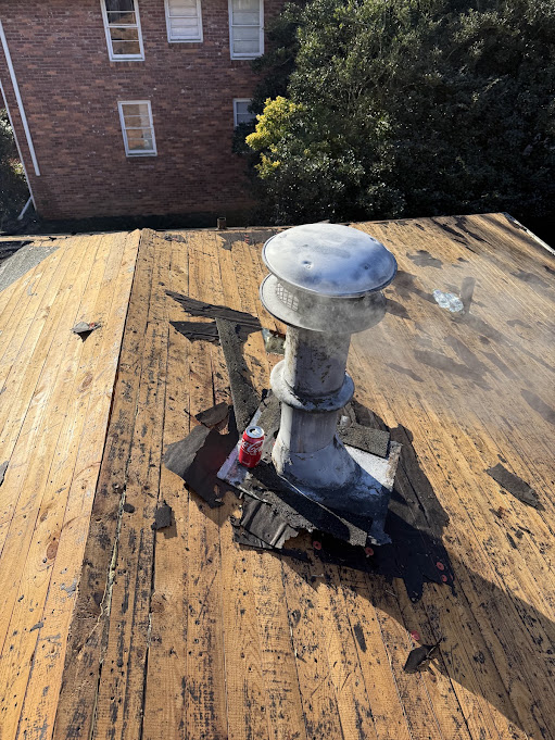 Shingles removed around a B-vent to expose the roof deck and the old flashing underneath