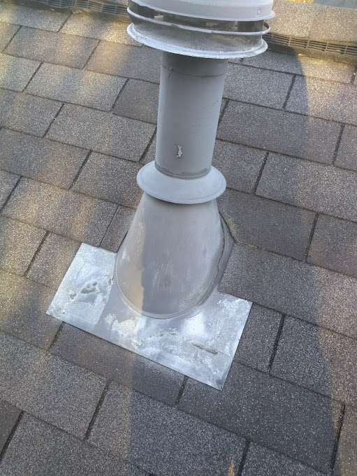 B-vent penetration inspected in place, showing the storm collar and sealed flashing base on the shingles