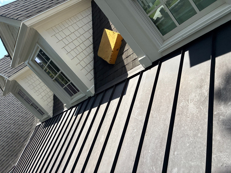 Dark standing seam panels running past cream lap siding and dormer windows