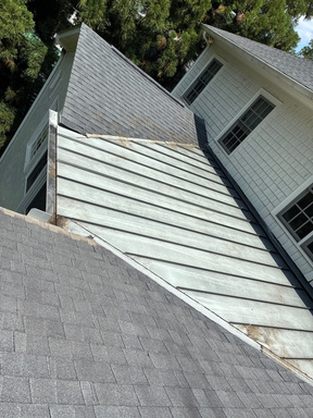 Light gray standing seam metal roof section meeting aging asphalt shingles on a cream sided two story home