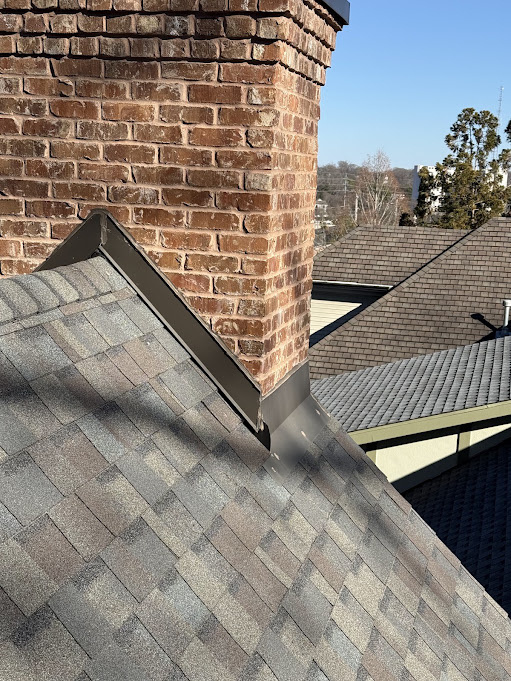 Brick chimney with new dark counter flashing stepping down where the wall meets the shingle roof