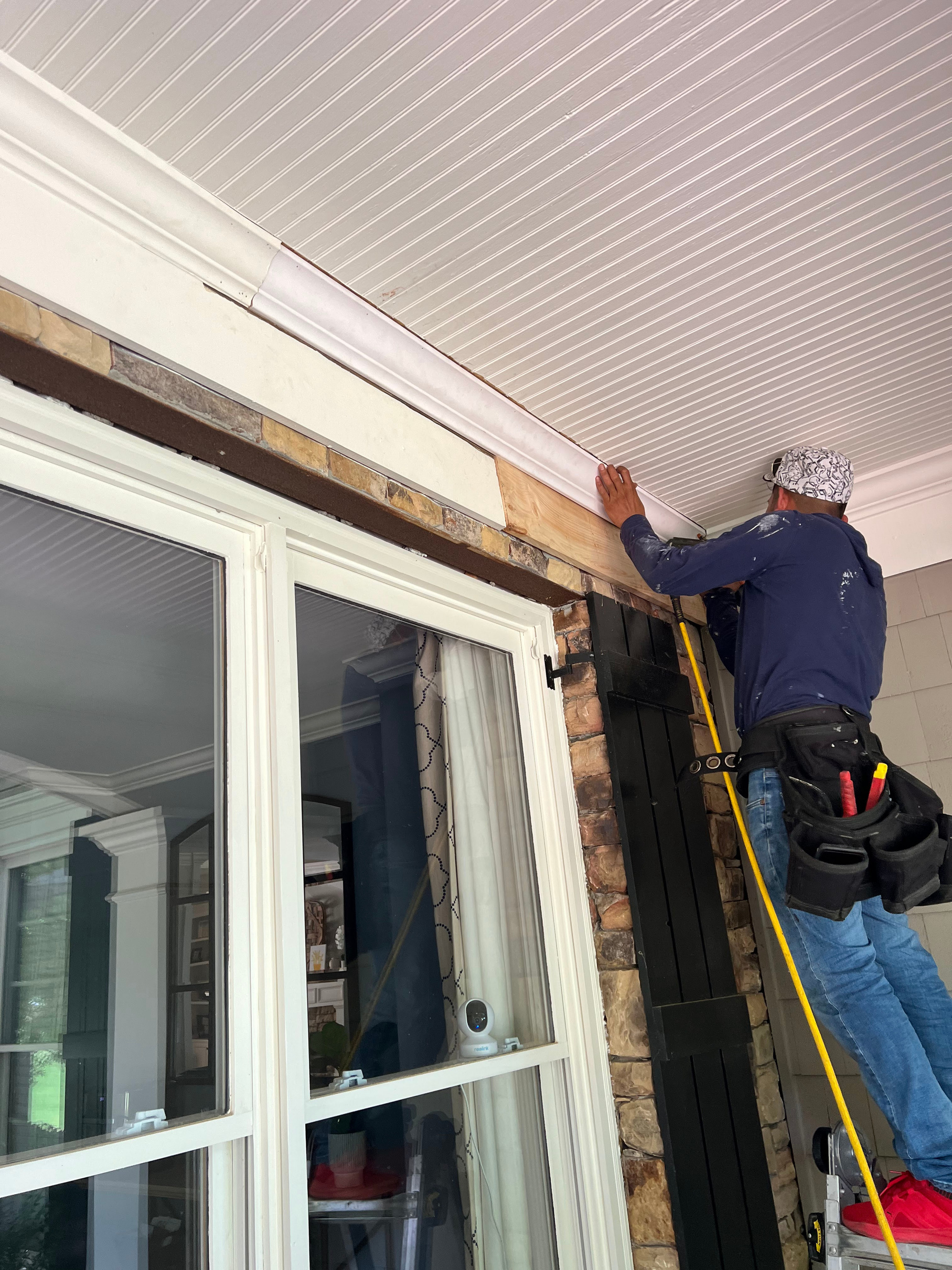 Technician on a ladder fitting new white soffit and trim above a window