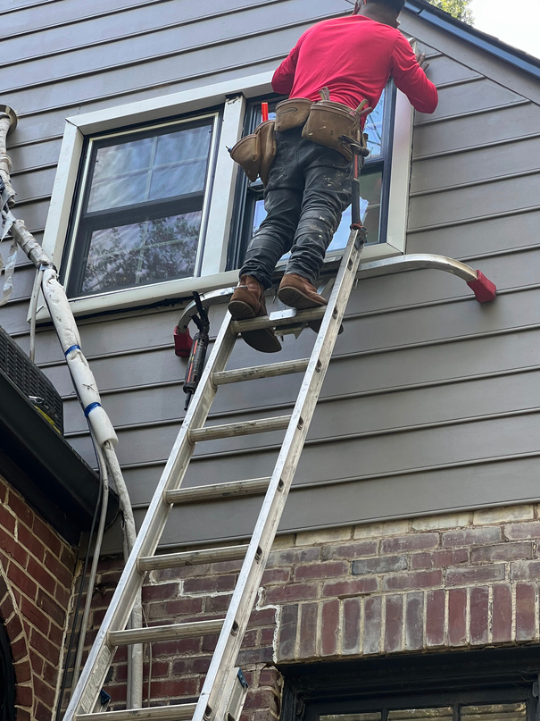 Technician on a ladder checking window trim on a gray sided home