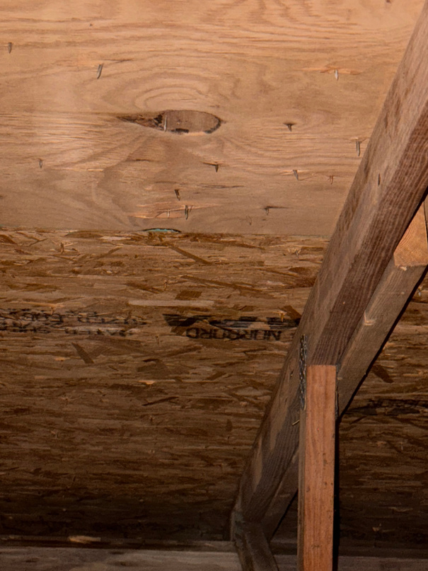 Underside of roof decking seen from the attic with water staining on the plywood and rafter