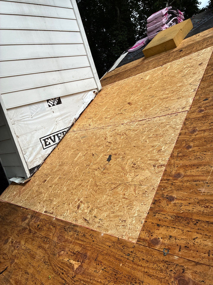 New OSB decking panel installed next to synthetic underlayment on a roof edge