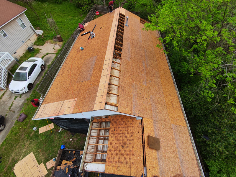Aerial view of a roof stripped to bare decking with crew and materials staged on the deck