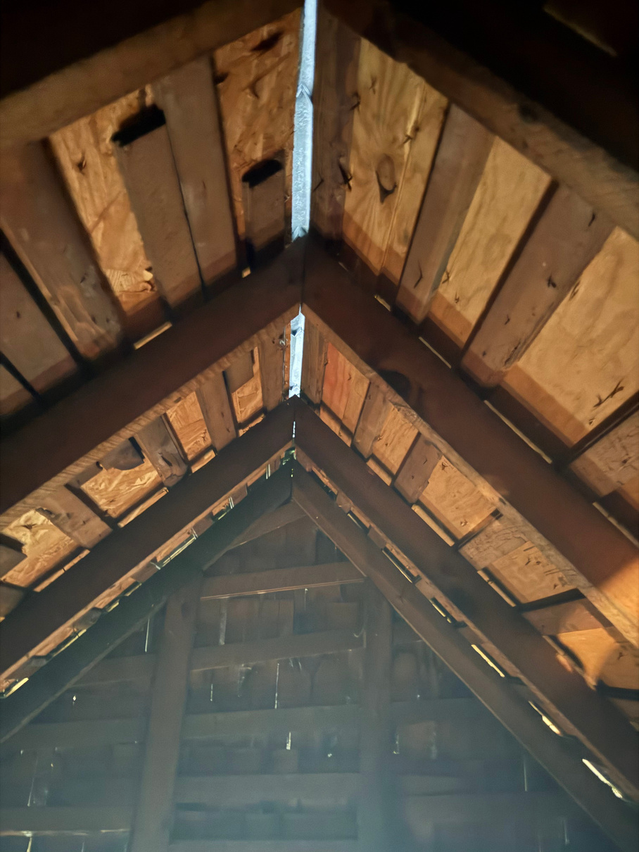 Inside view of an attic showing rafters and roof decking with sunlight coming through gaps