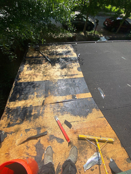 Flat roof stripped to bare decking with old membrane peeled back and tools laid out