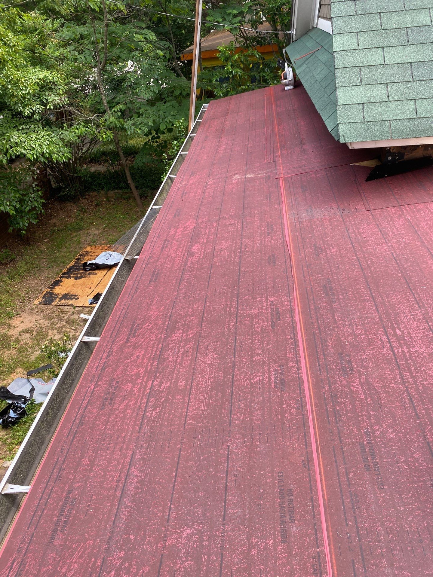 Long run of red rolled roofing membrane on a flat roof beside a green shingle gable