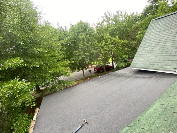 Finished dark gray flat roof membrane on a home addition, seen from above with trees behind