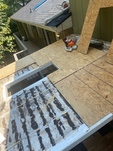 Old skylight flashing and asphalt patching exposed on a roof deck during tear-out