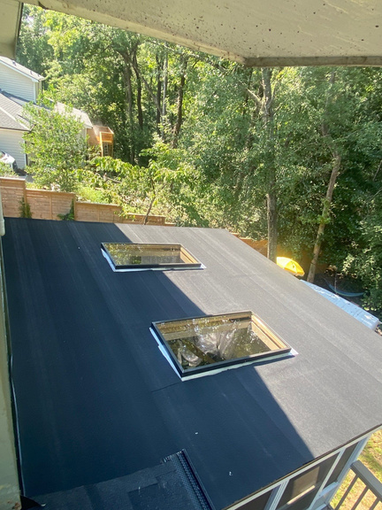 Two skylights set into a fresh black membrane roof over a covered porch