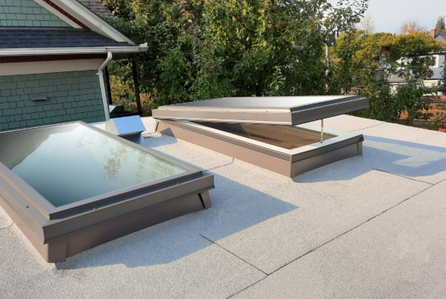Two new skylights installed on a white membrane flat roof beside a gray sided home