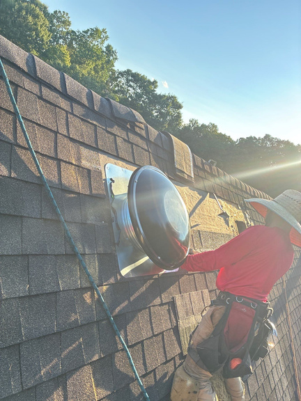 Technician on the roof with a dome attic fan in hand, checking the vent opening in the shingles