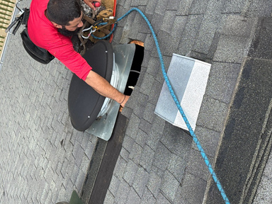Technician in a red shirt setting a new powered attic fan into a freshly cut and flashed roof opening