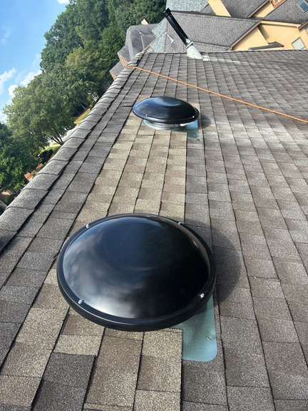 Black dome powered attic fan mounted on a gray shingle roof near the ridge
