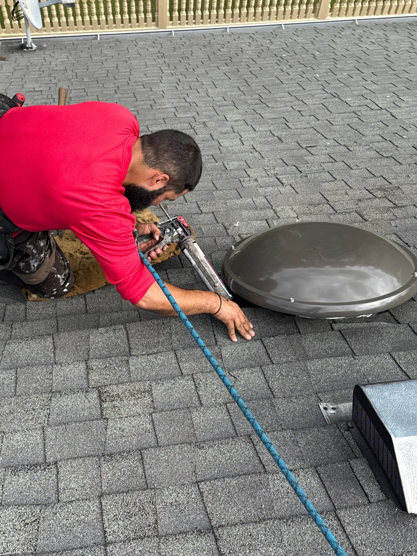 Shelter Guard technician in a red shirt fastening a new dome attic fan to a shingle roof