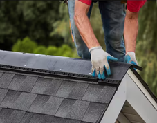 Worker installing shingles at the edge of a roof gable