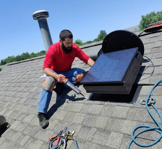 Technician installing a solar attic fan on a roof with tools