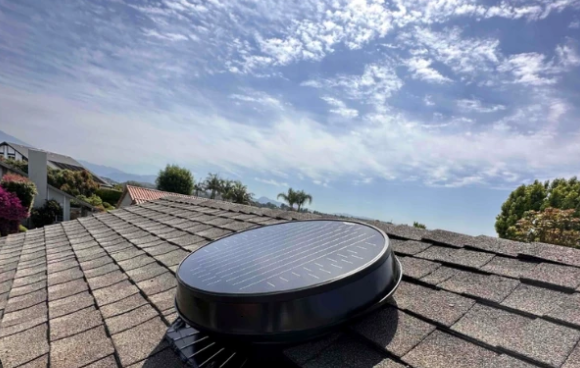 Solar attic fan mounted on a shingle roof under a clear sky