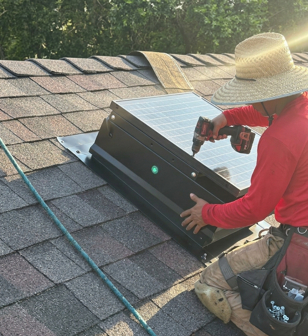 Technician mounting a solar attic fan panel on a shingle roof