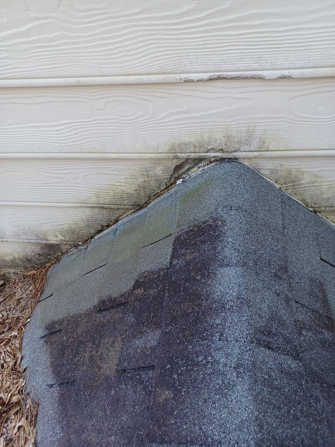 Close-up of damaged siding panels where shingles meet the wall, showing moisture staining and gap separation