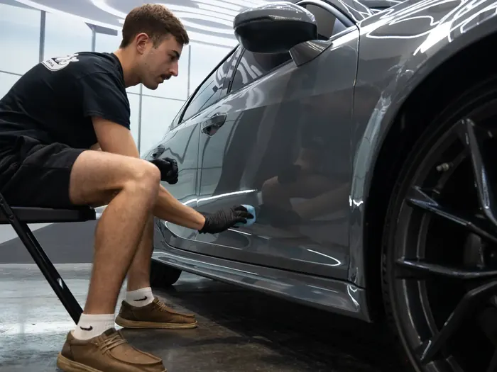 Technician applying ceramic coating to the side of a grey car