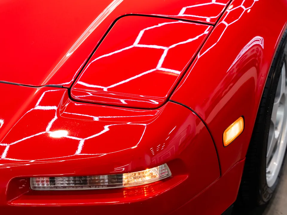 The hexagonal light ceiling reflected on the red paint of an Acura NSX