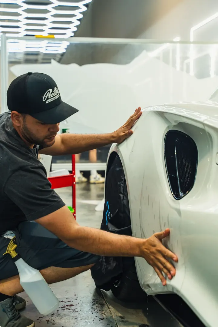 A technician smoothing paint protection film onto a white car