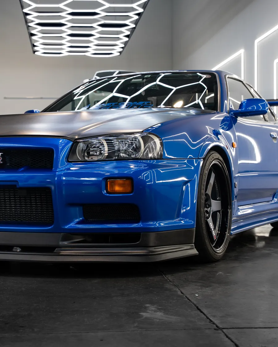 Bayside Blue Nissan Skyline GT-R V-spec under the hexagonal light ceiling, the hexagons reflected across its windshield