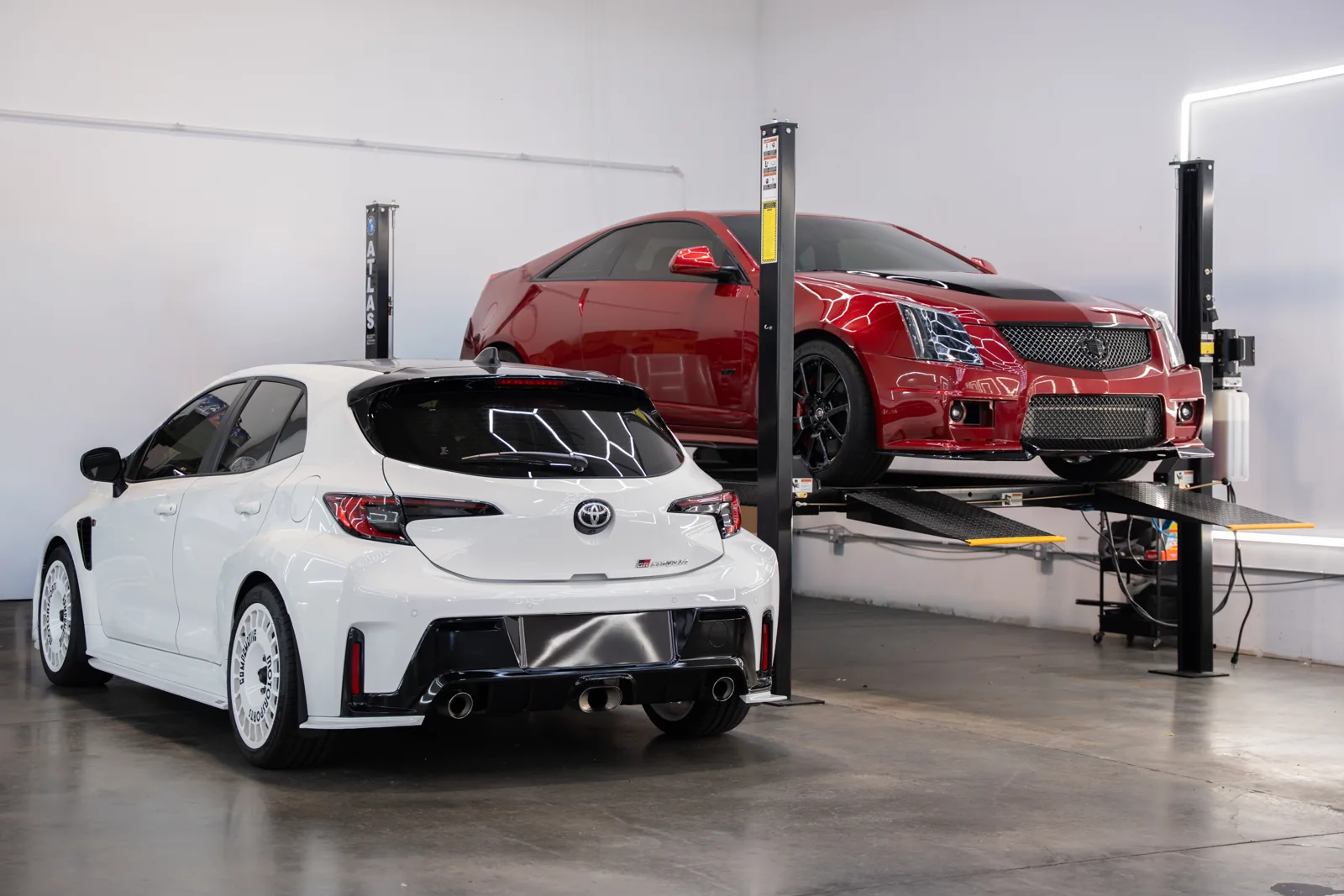 White hatchback and red sports car stored on lifts
