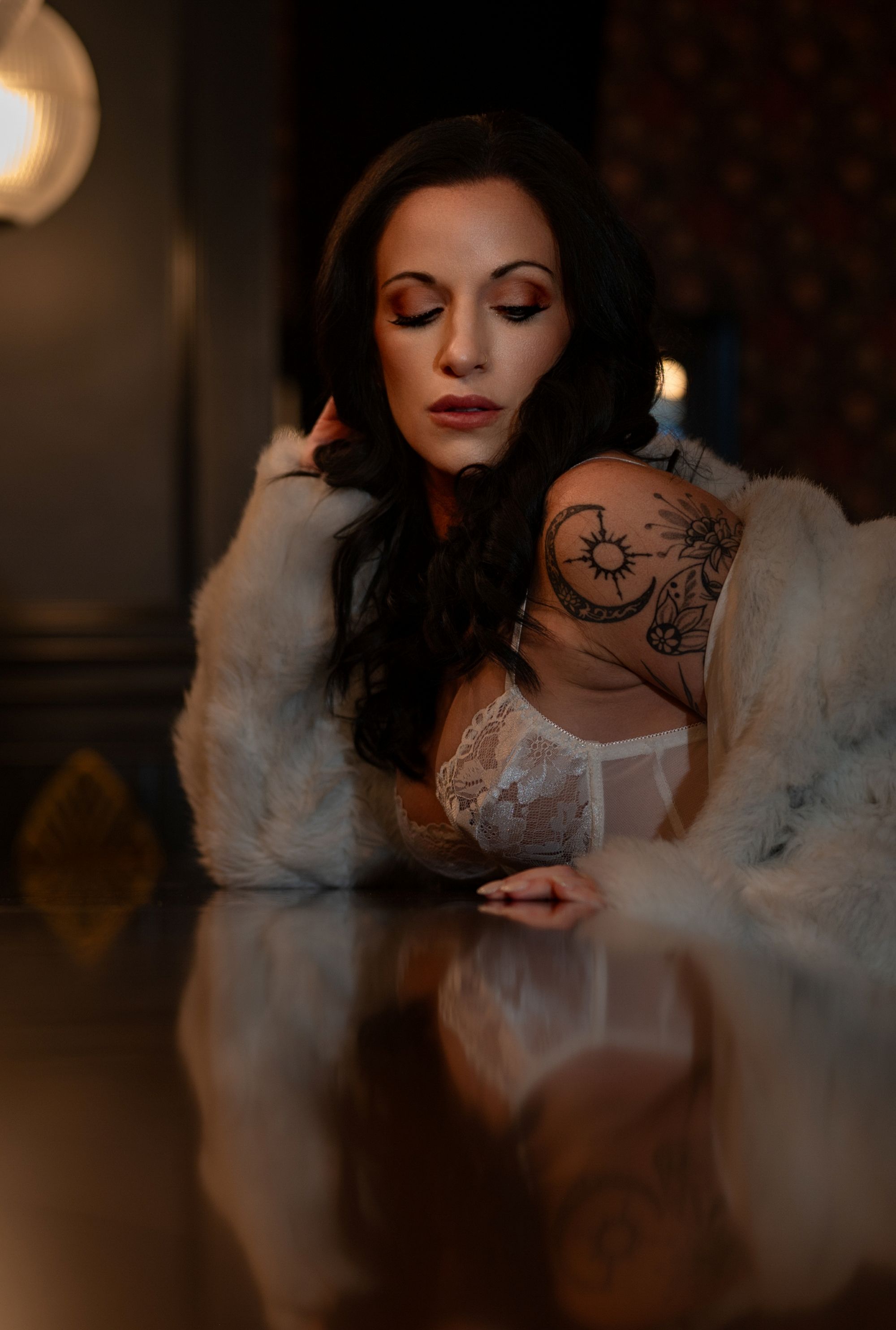 Luxury boudoir portrait of a tattooed woman in white lace lingerie and fur coat, posing with confidence and elegance.