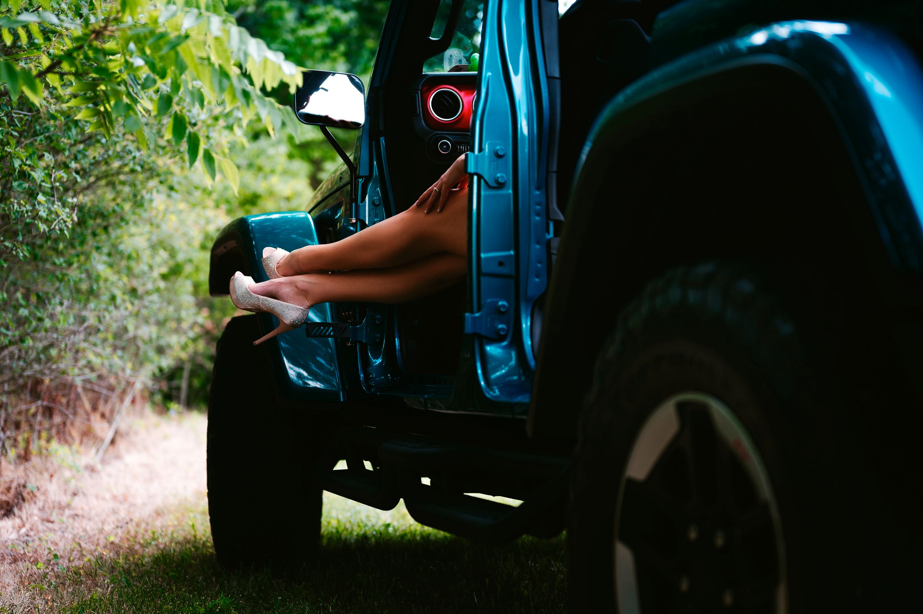 Stylish woman’s legs in sparkling high heels hanging out of a Jeep in a playful outdoor setting.