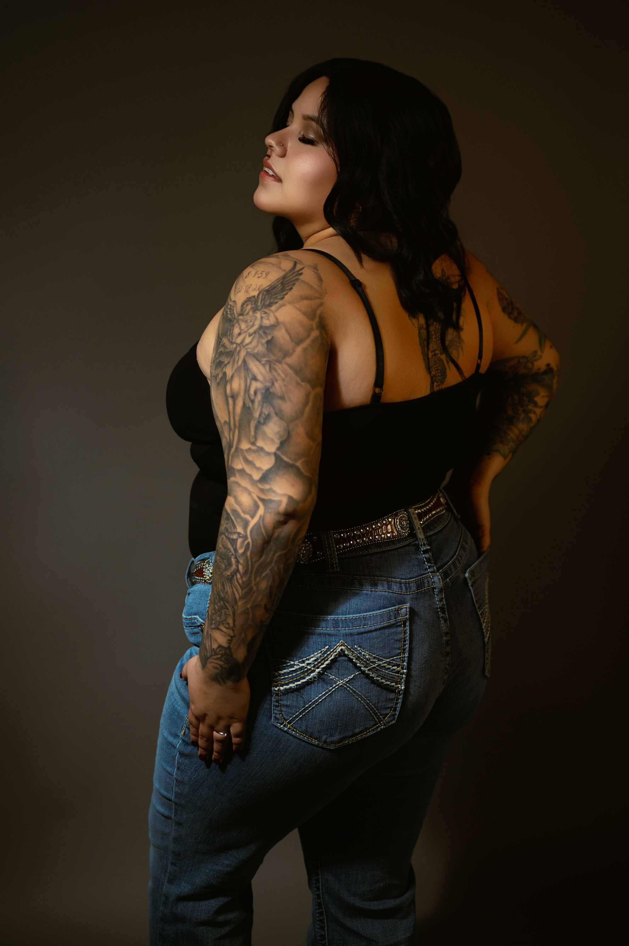 Confident portrait of a tattooed woman in jeans and a black top, showcasing her body art and style.