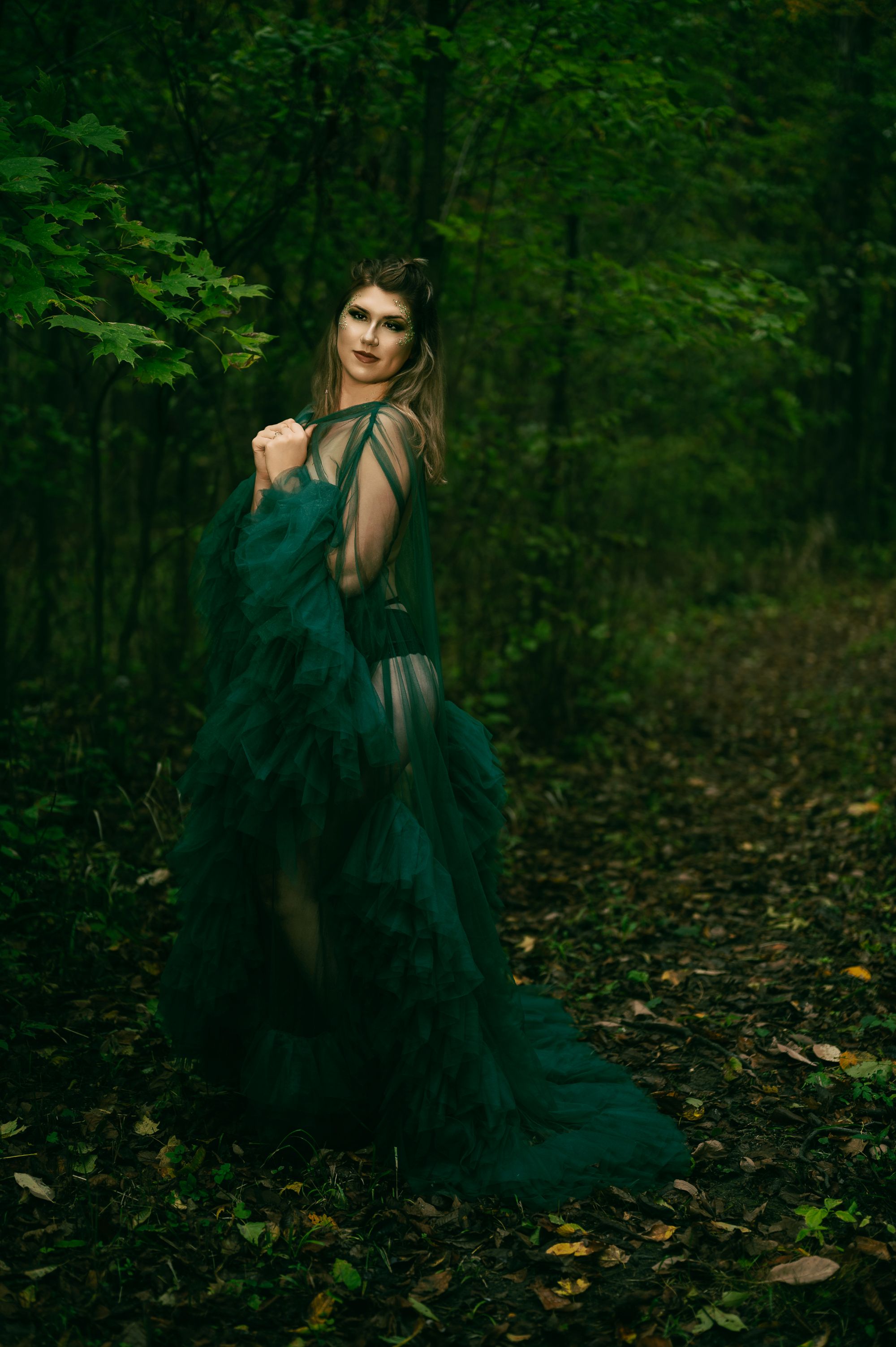 Editorial portrait of a woman in a dramatic green tulle gown posing in a lush forest setting.
