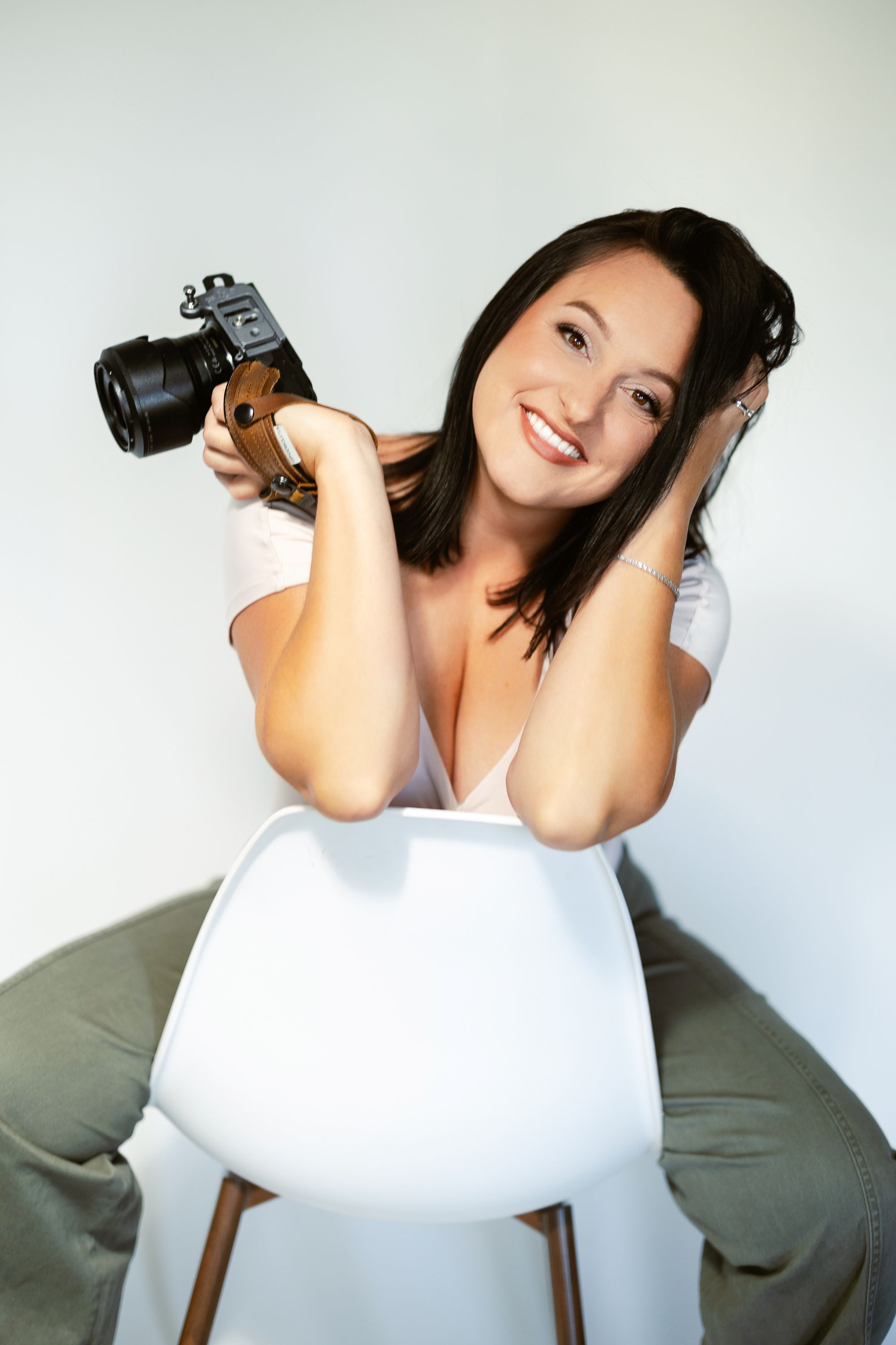 Professional photographer smiling with camera over shoulder while seated on modern chair