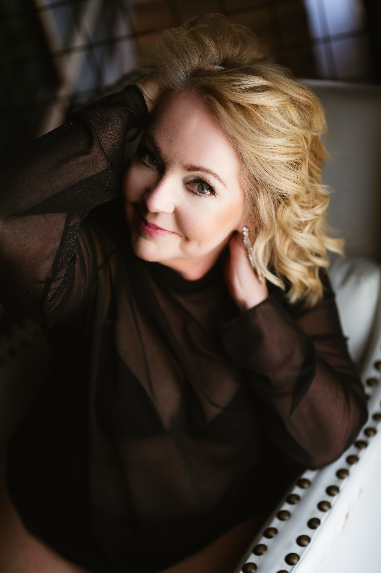 Boudoir portrait of woman in black sheer bodysuit posing confidently with soft smile