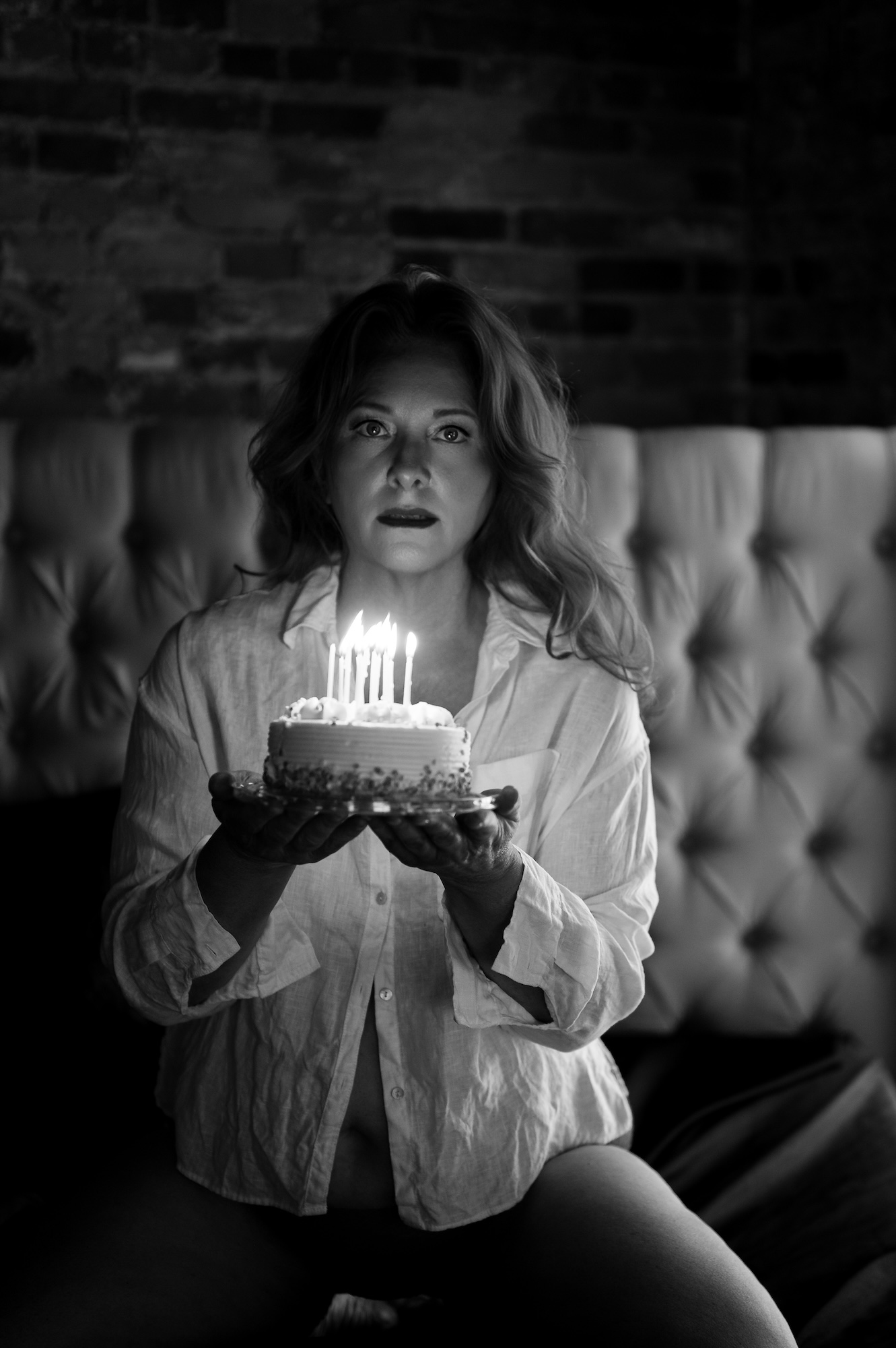 Creative boudoir photo of woman holding birthday cake with lit candles in dramatic black and white
