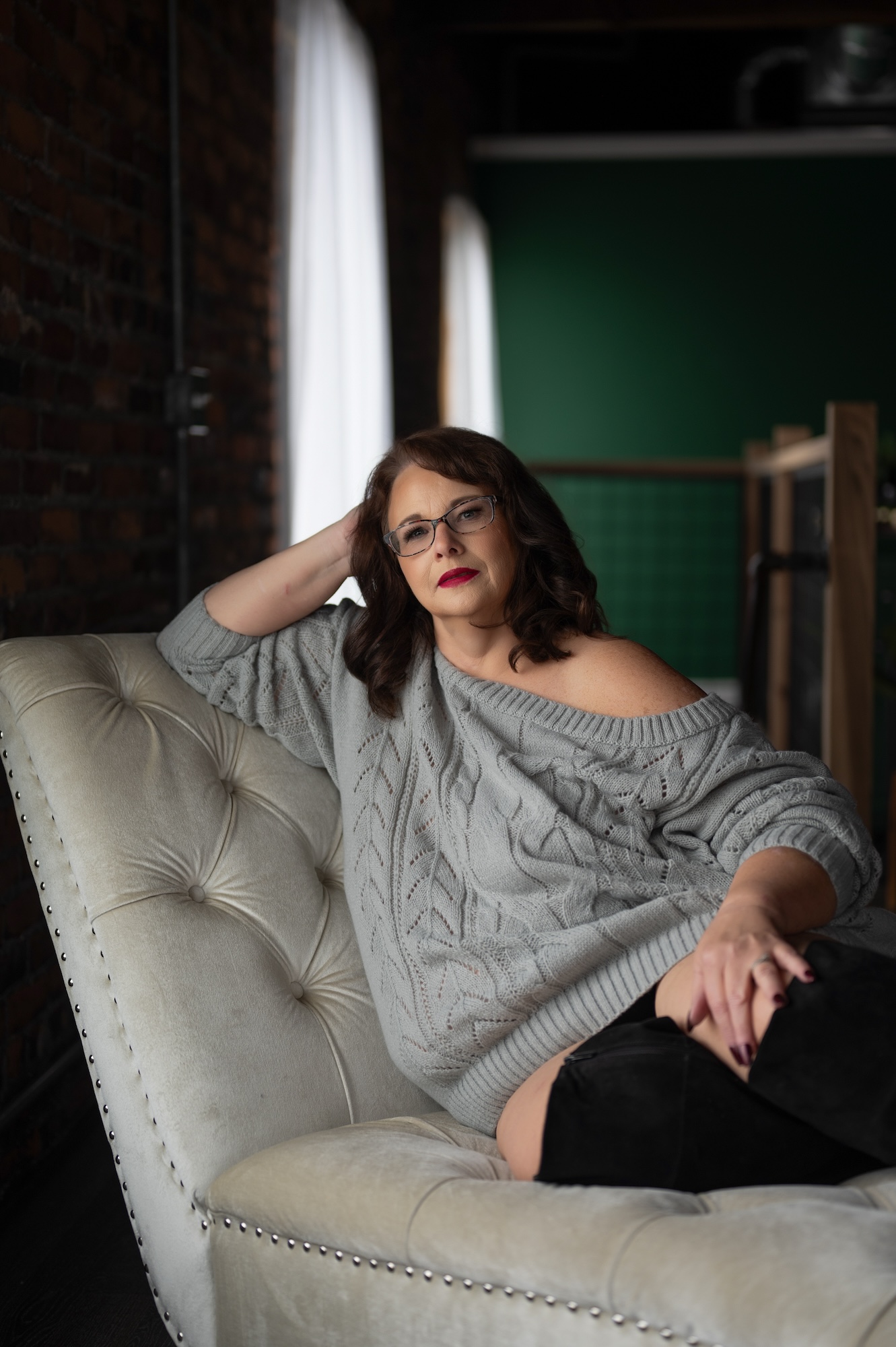 Boudoir portrait of mature woman in gray sweater lounging on velvet chaise