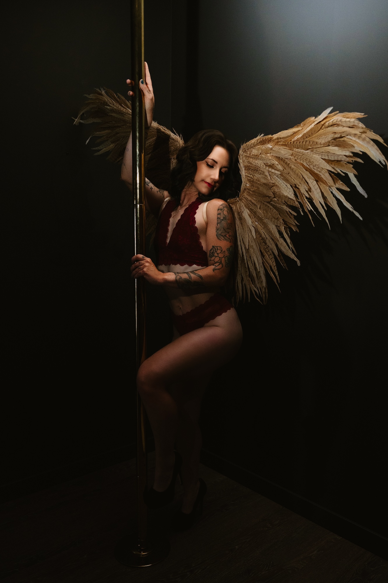 Artistic boudoir session with woman in red lingerie and angel wings posing by pole