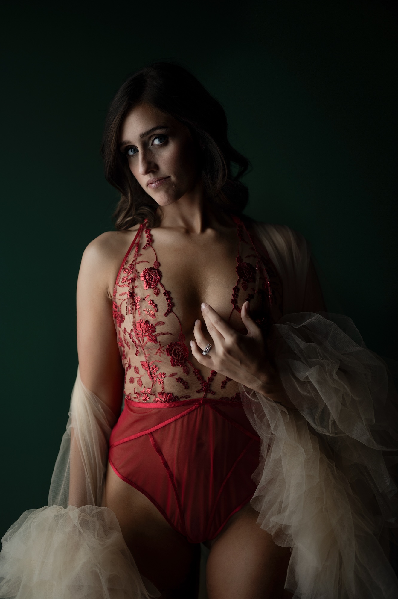 Boudoir portrait of woman in red floral lace bodysuit with sheer robe and moody lighting