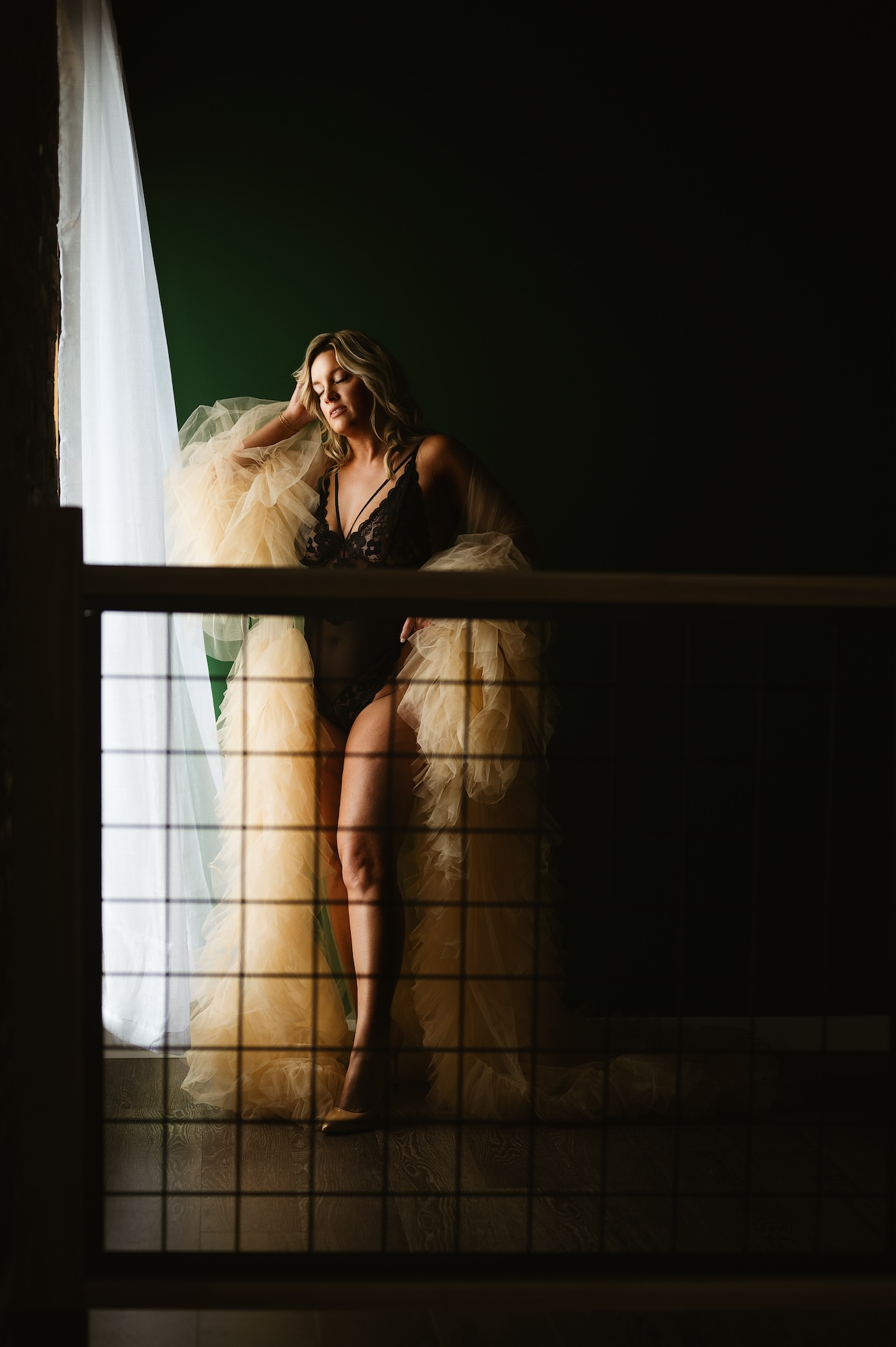 Boudoir photography of woman in black lace lingerie with flowing gold robe standing by window