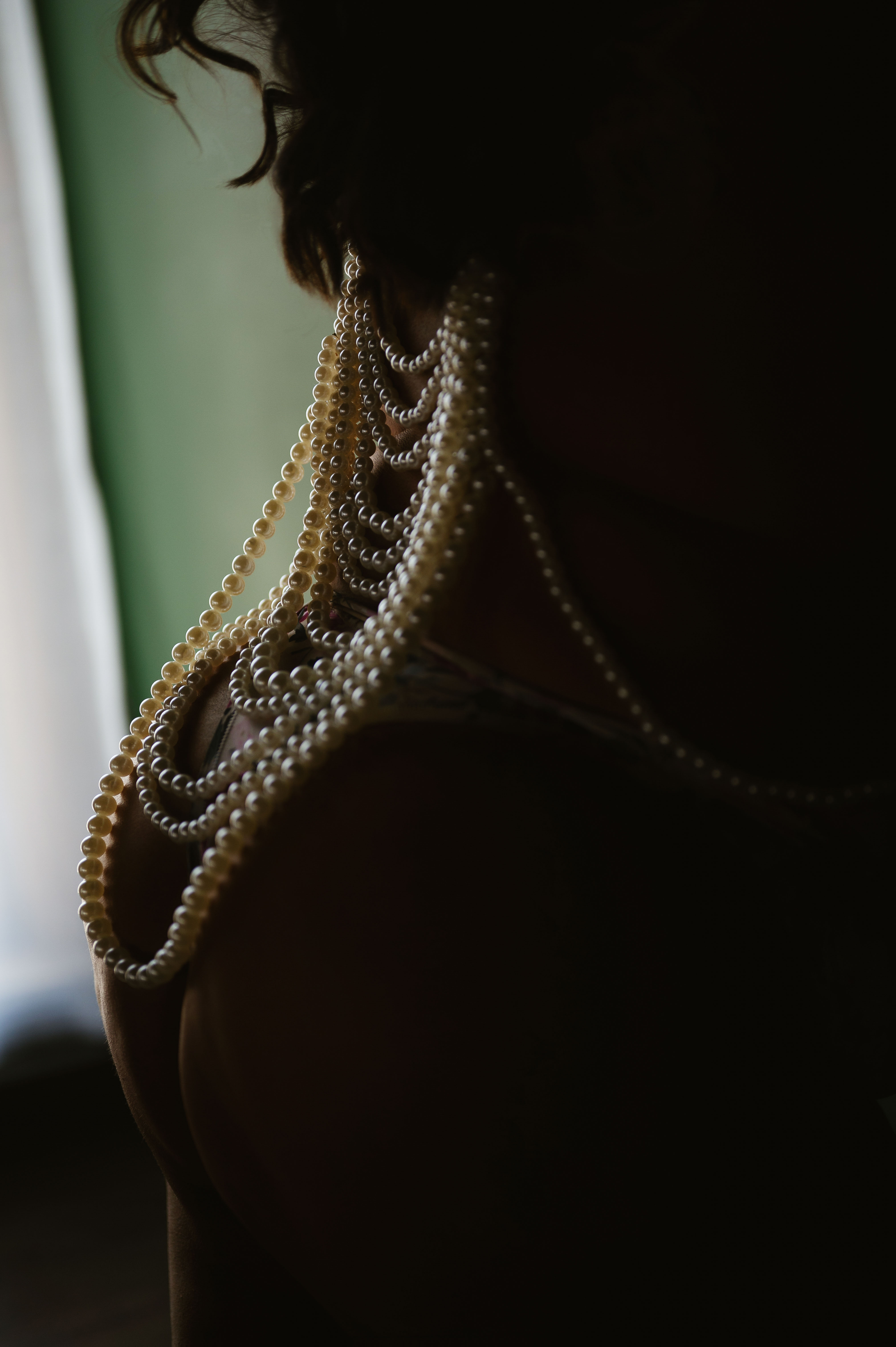 Close-up of a woman’s back adorned with layered pearl necklaces, softly lit to highlight the texture and curves.