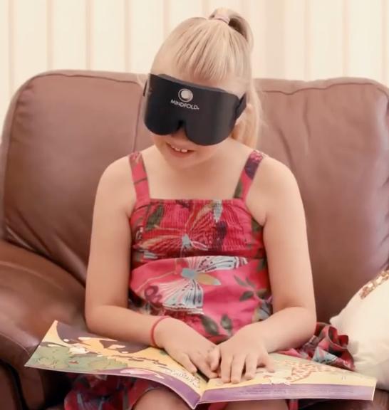 A sighted girl reading a picture book while wearing a training mask